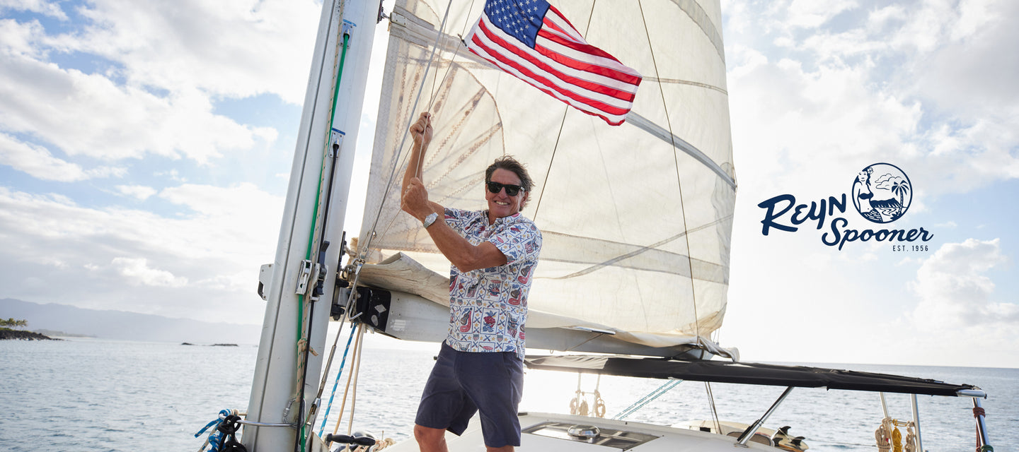 Man on a boat wearing a white aloha shirt with USA flags on it while raising up the American flag