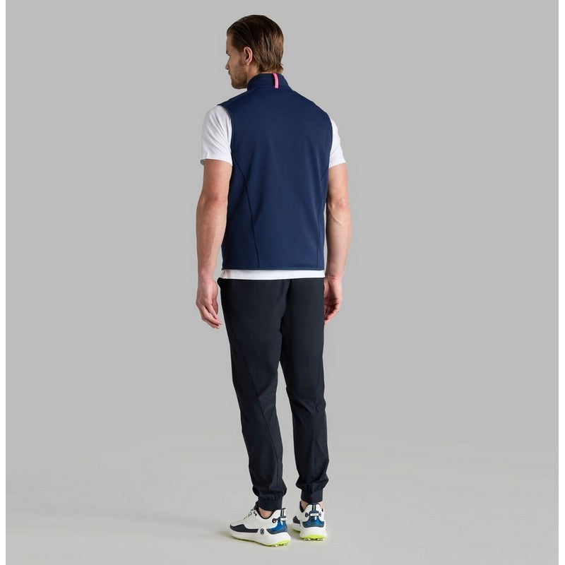 Man wearing a navy vest over a white shirt and dark pants on a gray background