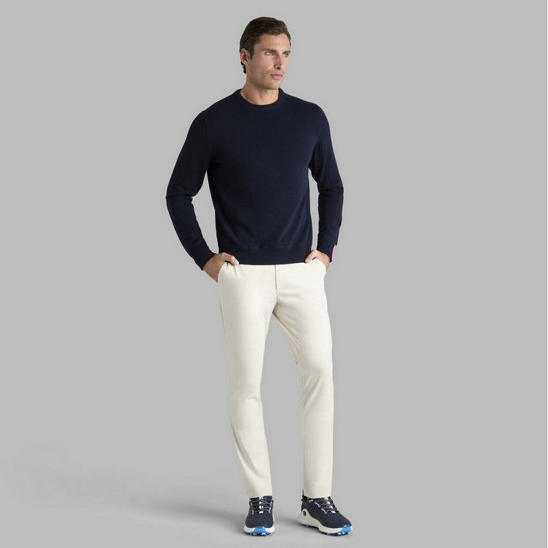 Man wearing a navy sweater and white pants on a gray background
