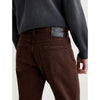 Rear view of a person wearing dark brown denim jeans and a dark charcoal sweatshirt, showing the back pocket and waistband label.