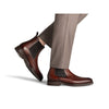 Brown leather shoes with black accents worn with beige pants on a white background
