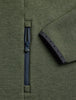 Close-up of an olive green knit garment showing a dark navy zipper and a matching navy sleeve cuff with small decorative dots.