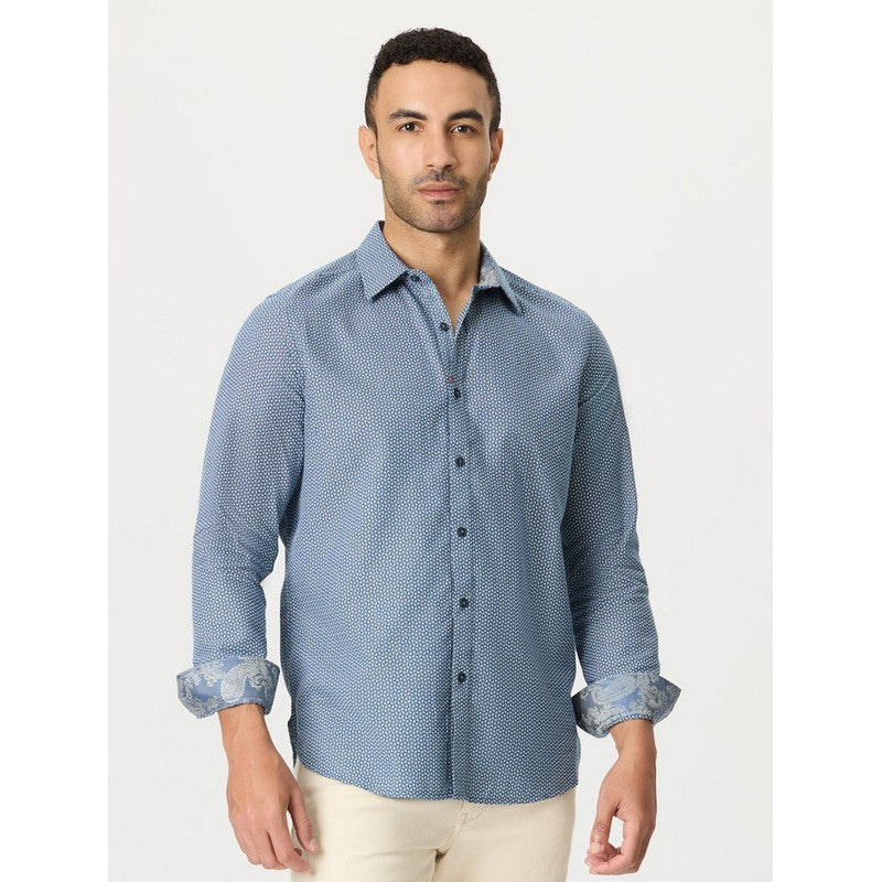 A man wearing a light blue long-sleeve button-down shirt with a subtle micro-pattern and rolled-up sleeves, paired with beige trousers, against a plain light gray background.