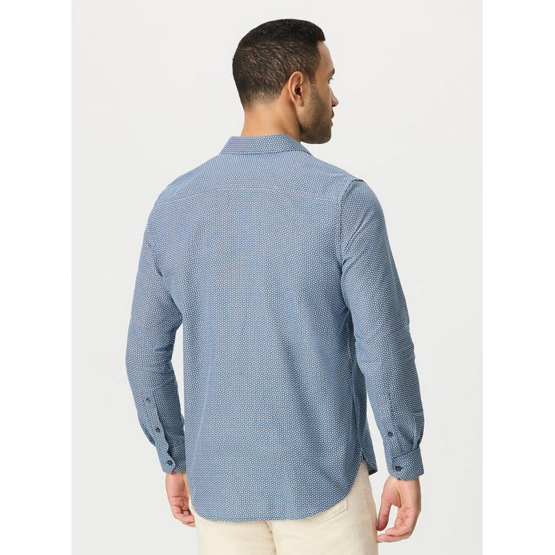 A man viewed from the back wearing a light blue patterned long-sleeve button-up shirt and cream pants, set against a plain light gray studio background.