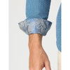 Close-up of a person's forearm and hand wearing a blue patterned dress shirt with a rolled cuff showing a paisley-patterned lining.