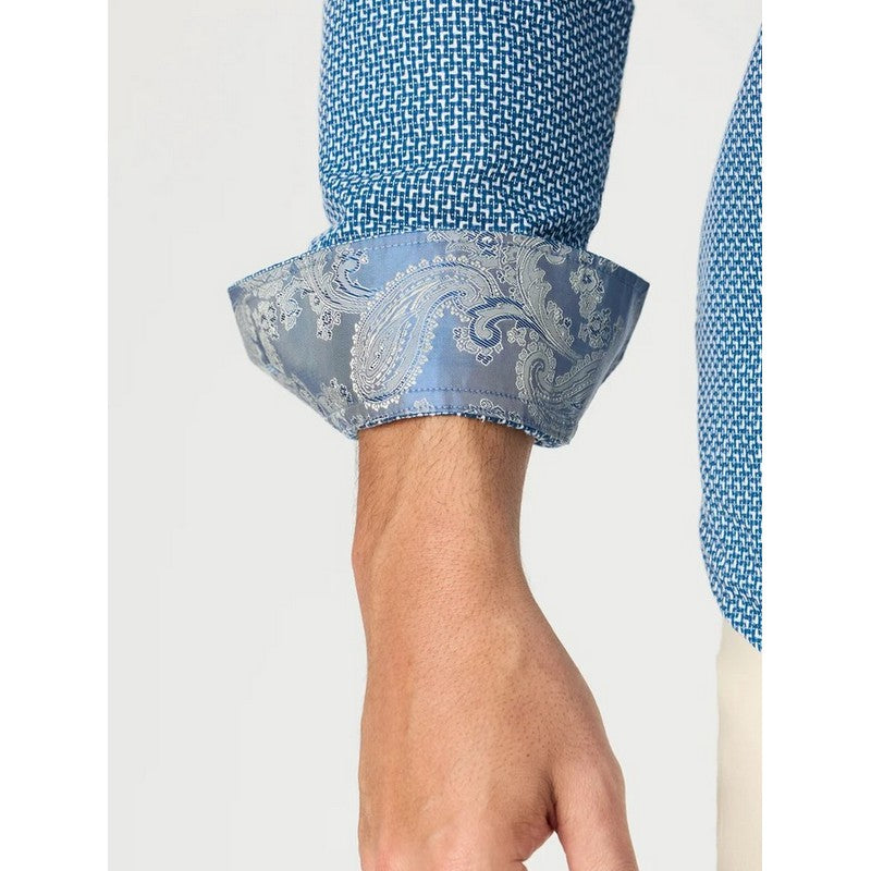 Close-up of a person's forearm and hand wearing a blue patterned dress shirt with a rolled cuff showing a paisley-patterned lining.