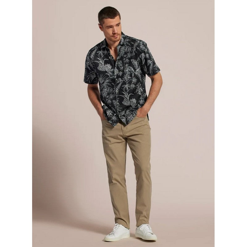 Man wearing a patterned shirt and beige pants against a beige background