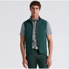 A man modeling a dark green sleeveless zip-front vest over a black and white striped polo shirt, paired with matching dark green trousers, against a light gray studio background.