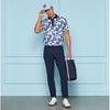 Person wearing a blue and white floral shirt with navy pants, holding a golf bag against a light blue wall.