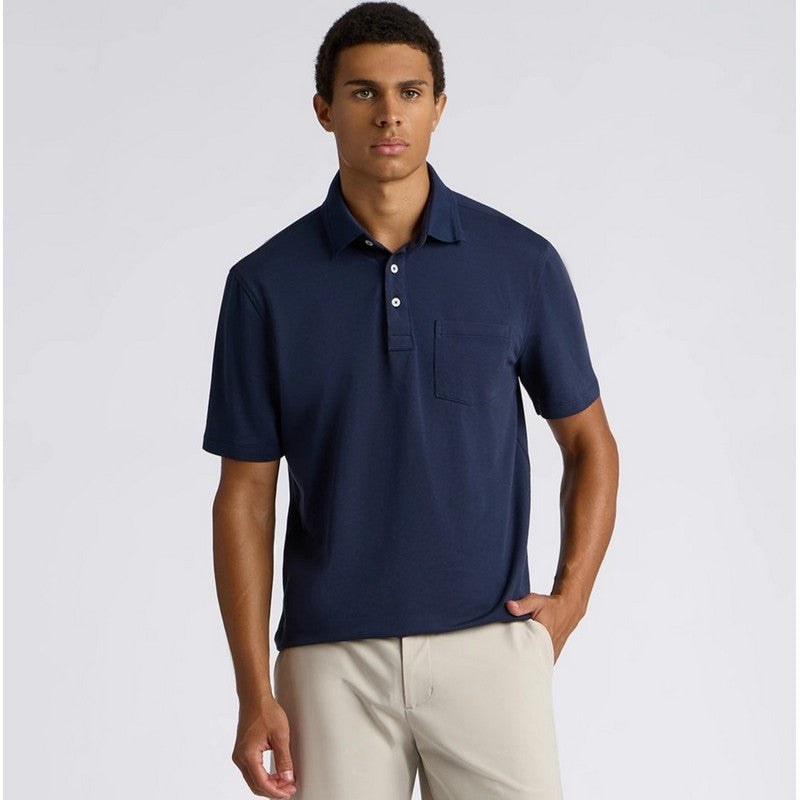 A man wearing a navy blue short-sleeve polo shirt with a chest pocket, paired with light beige trousers, standing against a light gray studio background.