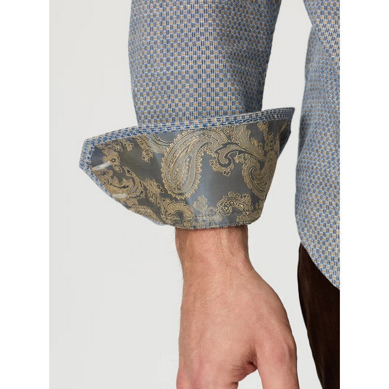 Close-up of a person's wrist and hand wearing a patterned dress shirt with rolled cuffs showing a paisley lining in blue and gold.