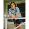 Man in a blue floral shirt and navy shorts leaning on a railing outdoors.