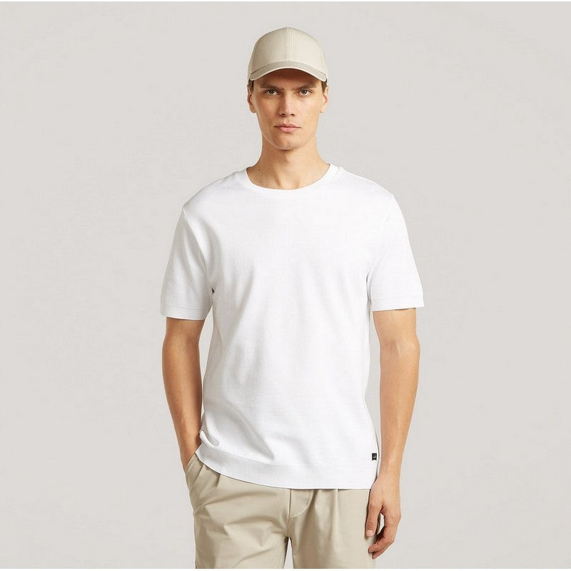 Man wearing a white t-shirt, beige cap, and pants on a light gray background