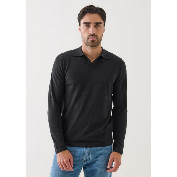 Man wearing a black long-sleeve polo shirt and blue jeans on a white background