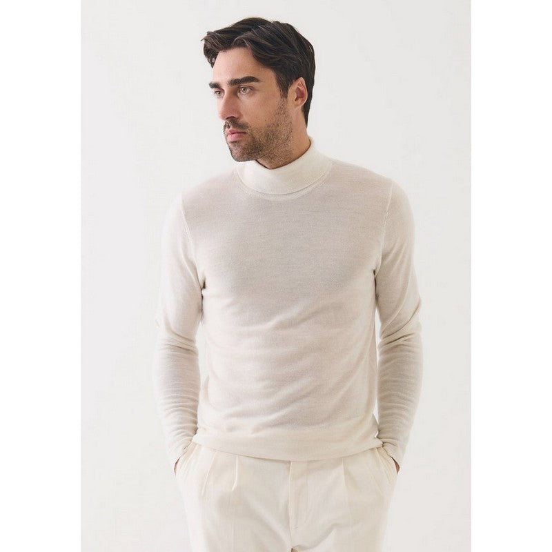 Man wearing a white turtleneck sweater and pants against a light background