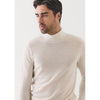 Man wearing a beige turtleneck sweater against a white background