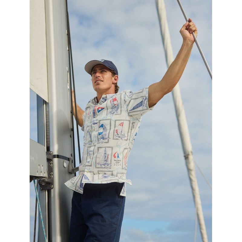Person on a sailboat with a patterned shirt and cap, against a blue sky.