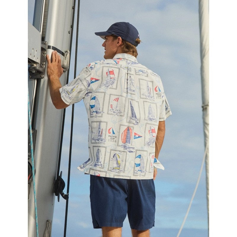 Man on a sailboat wearing a patterned shirt and navy cap with a blue sky background