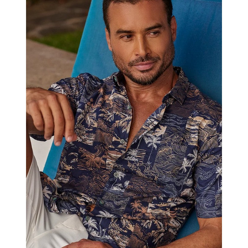 Man wearing a patterned shirt sitting on a blue chair.