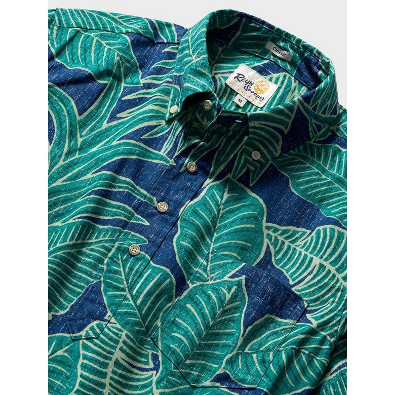 A close-up of a men's button-down shirt with a bold tropical leaf pattern in teal green and dark blue, featuring a pointed collar and visible brand label.