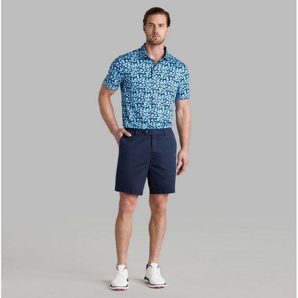 Man wearing a blue patterned polo shirt and navy shorts on a gray background
