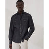 Man wearing a dark denim shirt with white pants on a plain background