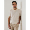 Man wearing a beige textured shirt and pants against a white wall