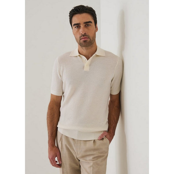 Man wearing a beige textured shirt and pants against a white wall