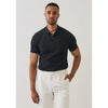 Man wearing a black polo shirt and white pants against a plain background