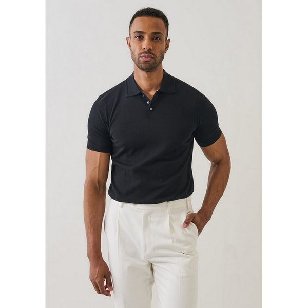Man wearing a black polo shirt and white pants against a plain background