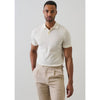 Man wearing a white polo shirt and beige pants against a plain background