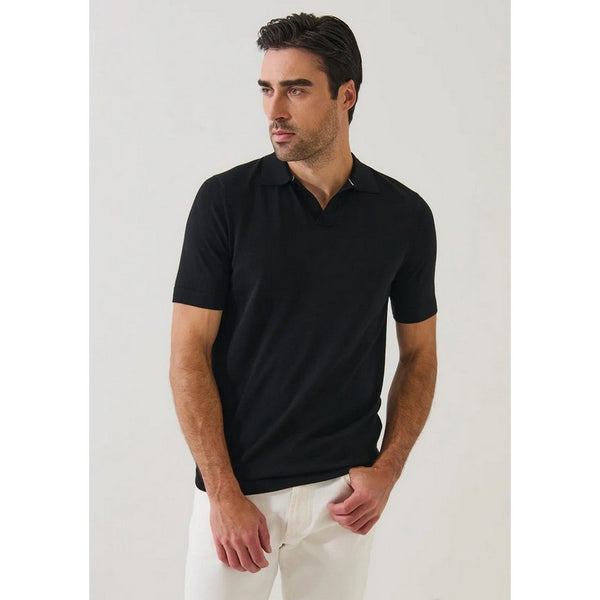 Man wearing a black polo shirt and white pants against a light gray background